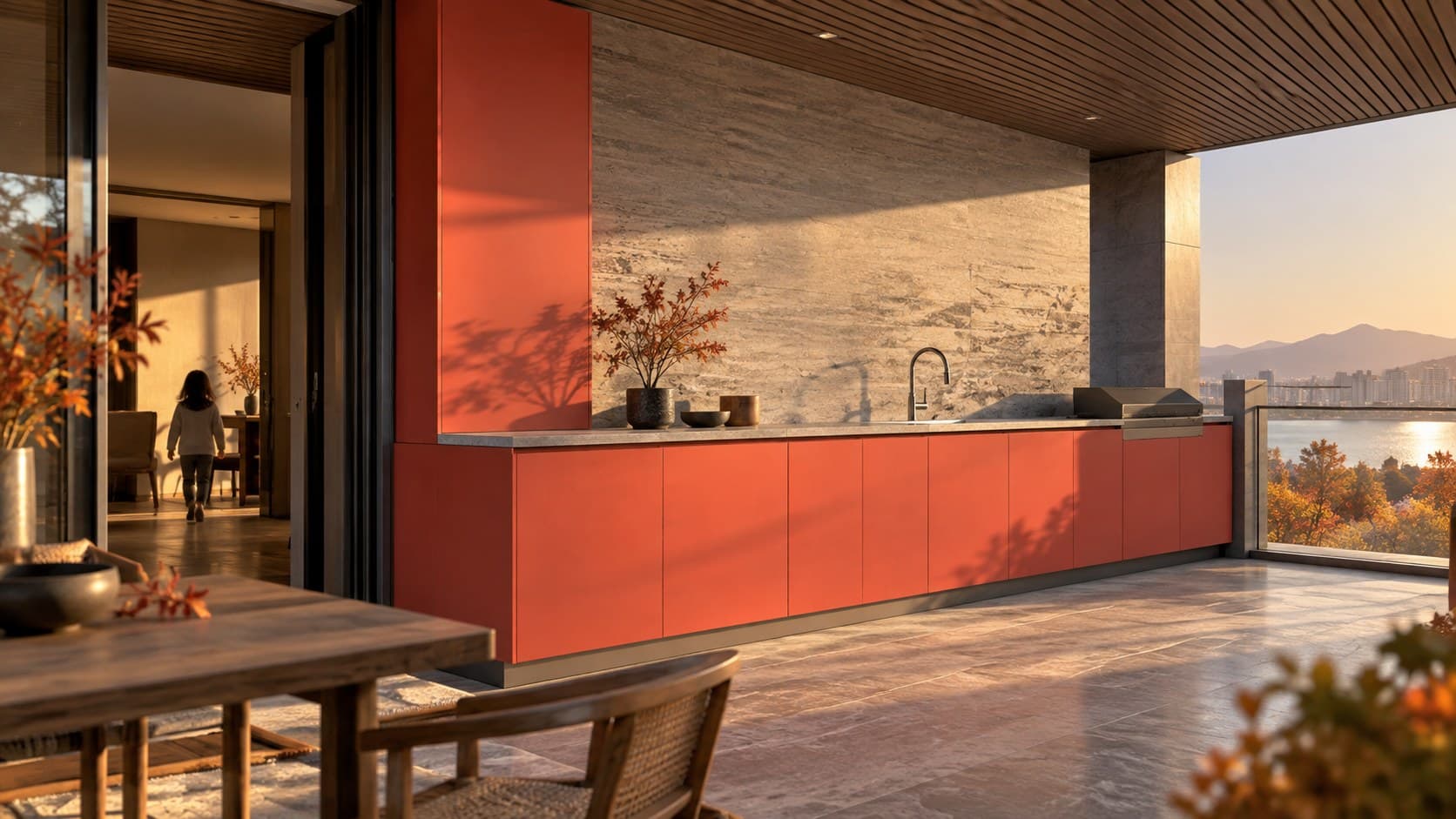 Sheltered balcony with coral red powder-coated 304 stainless steel outdoor cabinetry and a stone worktop in golden autumn light