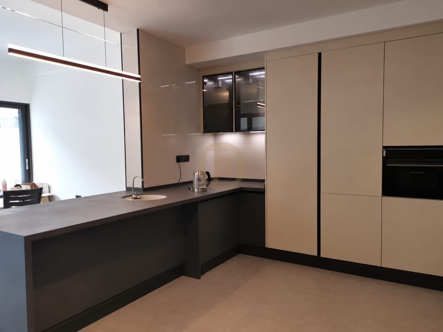 Charcoal peninsula with a round sink facing cream tall cabinets and a built-in oven