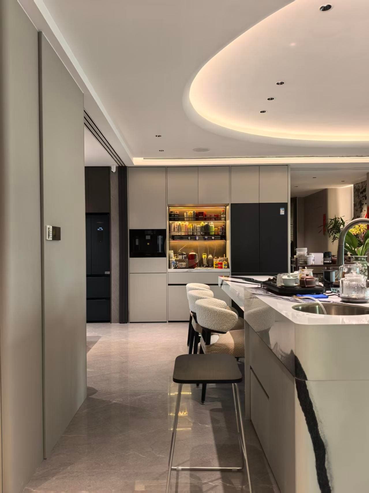 Pared de muebles claros junto al comedor con estantes iluminados, cajones, encimera y fregadero