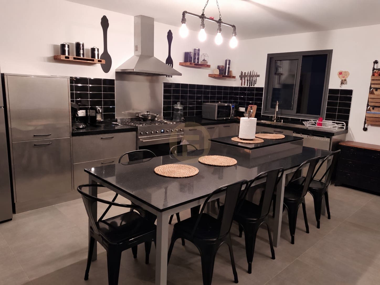 Stainless steel kitchen with black subway tiles and a black stone island dining table at night
