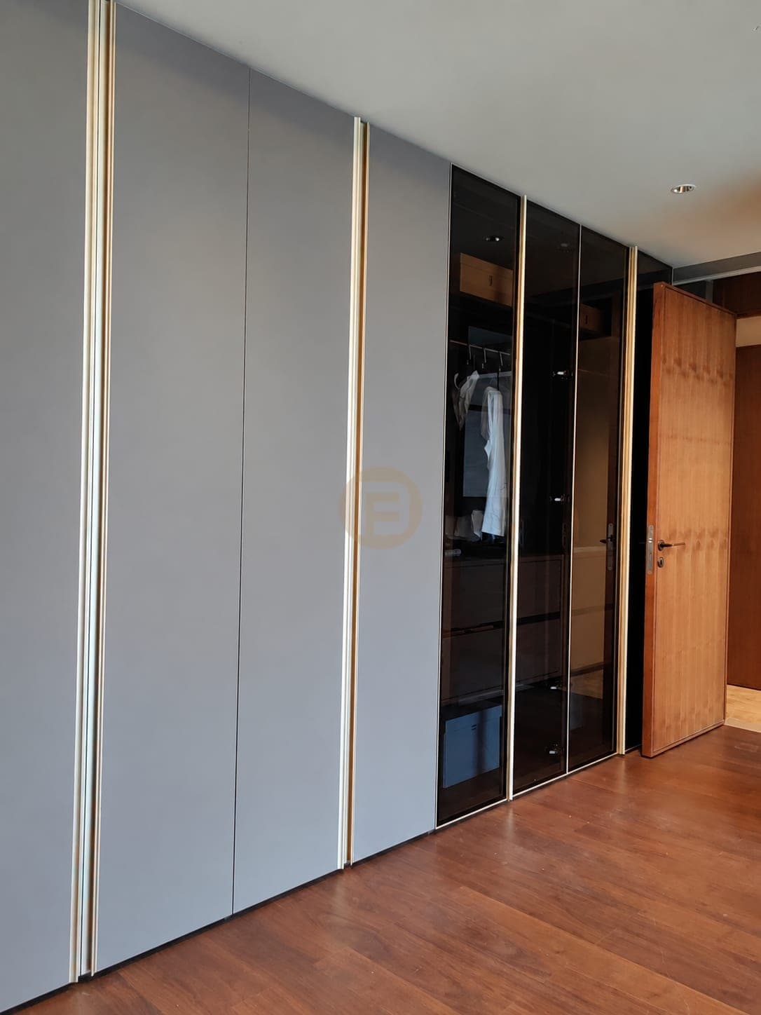 Pared de armarios grises de dormitorio con perfiles de tono bronce y puertas de vidrio ahumado