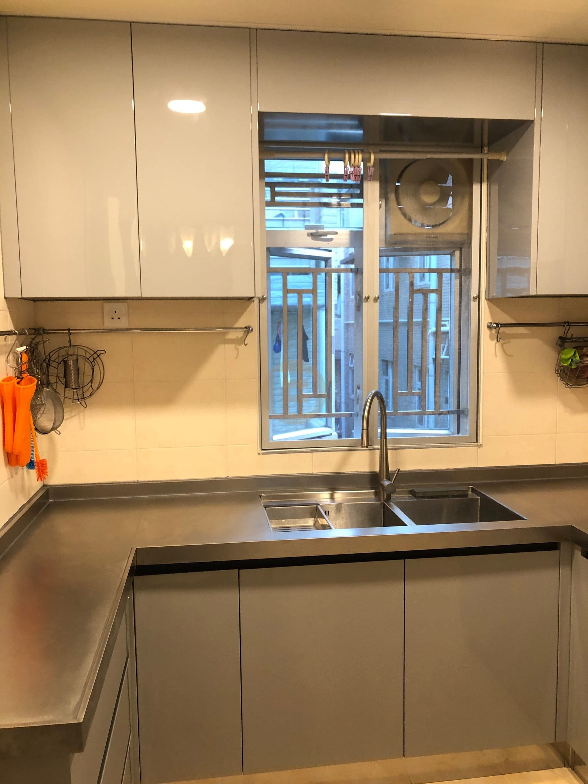 Double sink under the window between grey gloss wall cabinets and stainless worktops