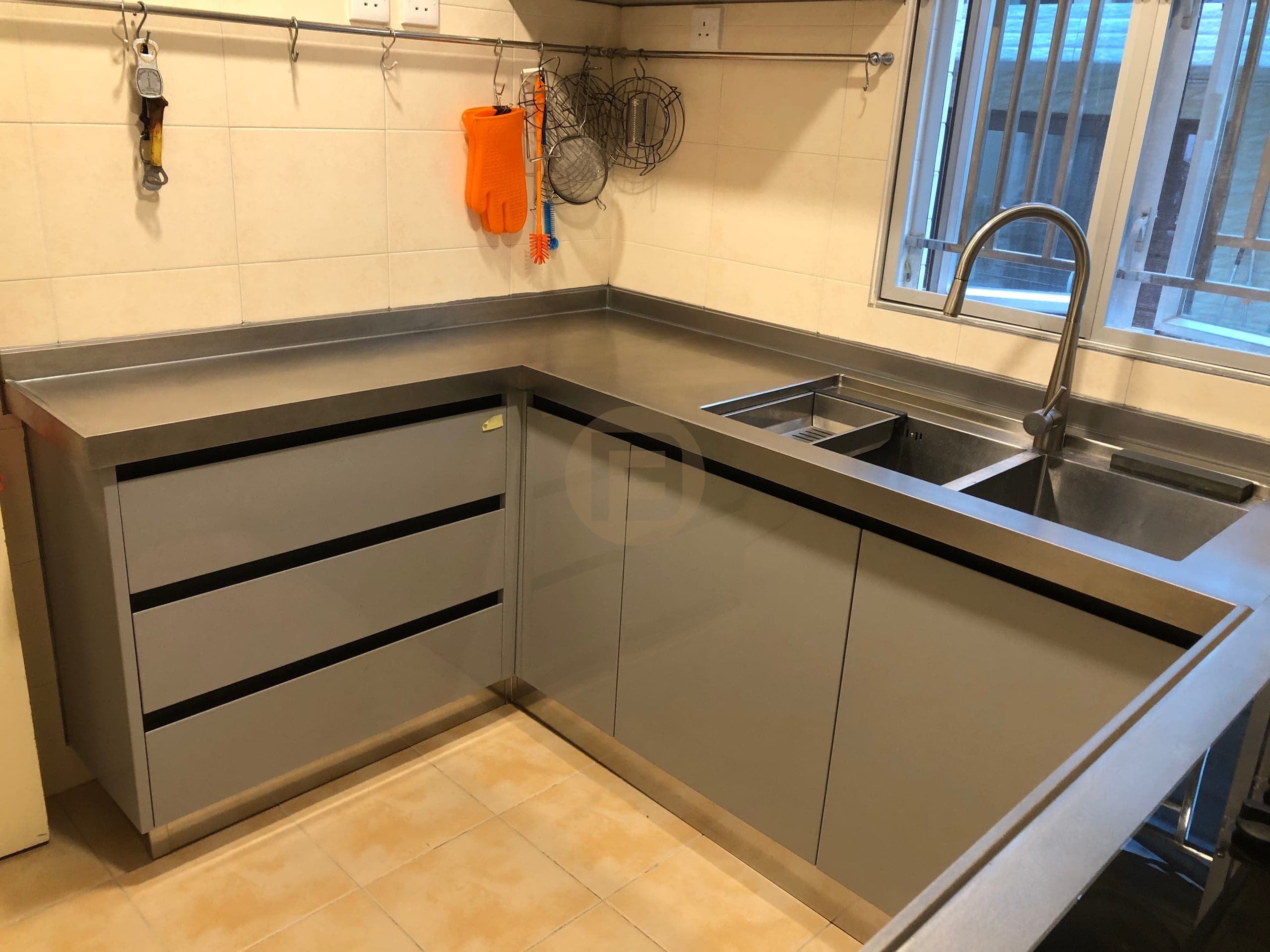 Grey drawers and doors below an L-shaped stainless steel worktop with an integrated sink