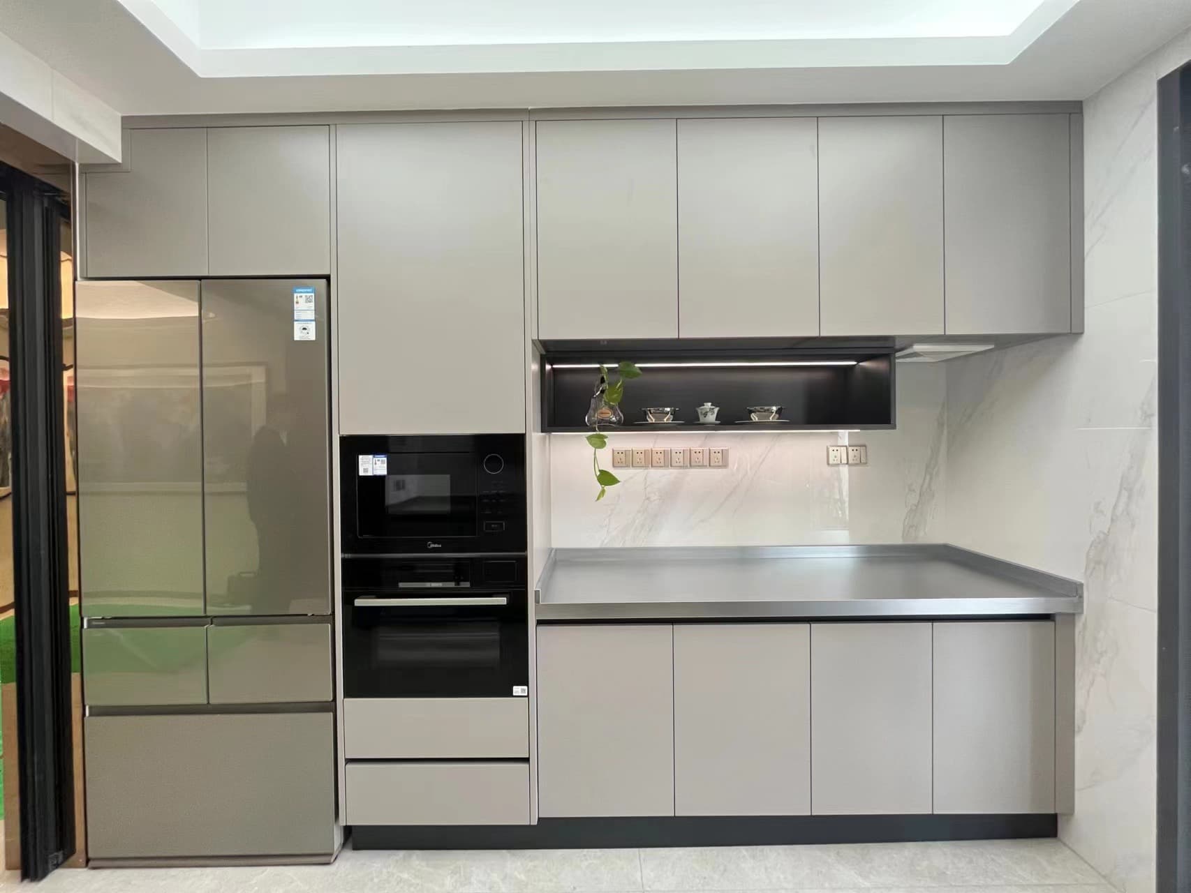 Tall refrigerator and oven wall beside a lit recessed display shelf