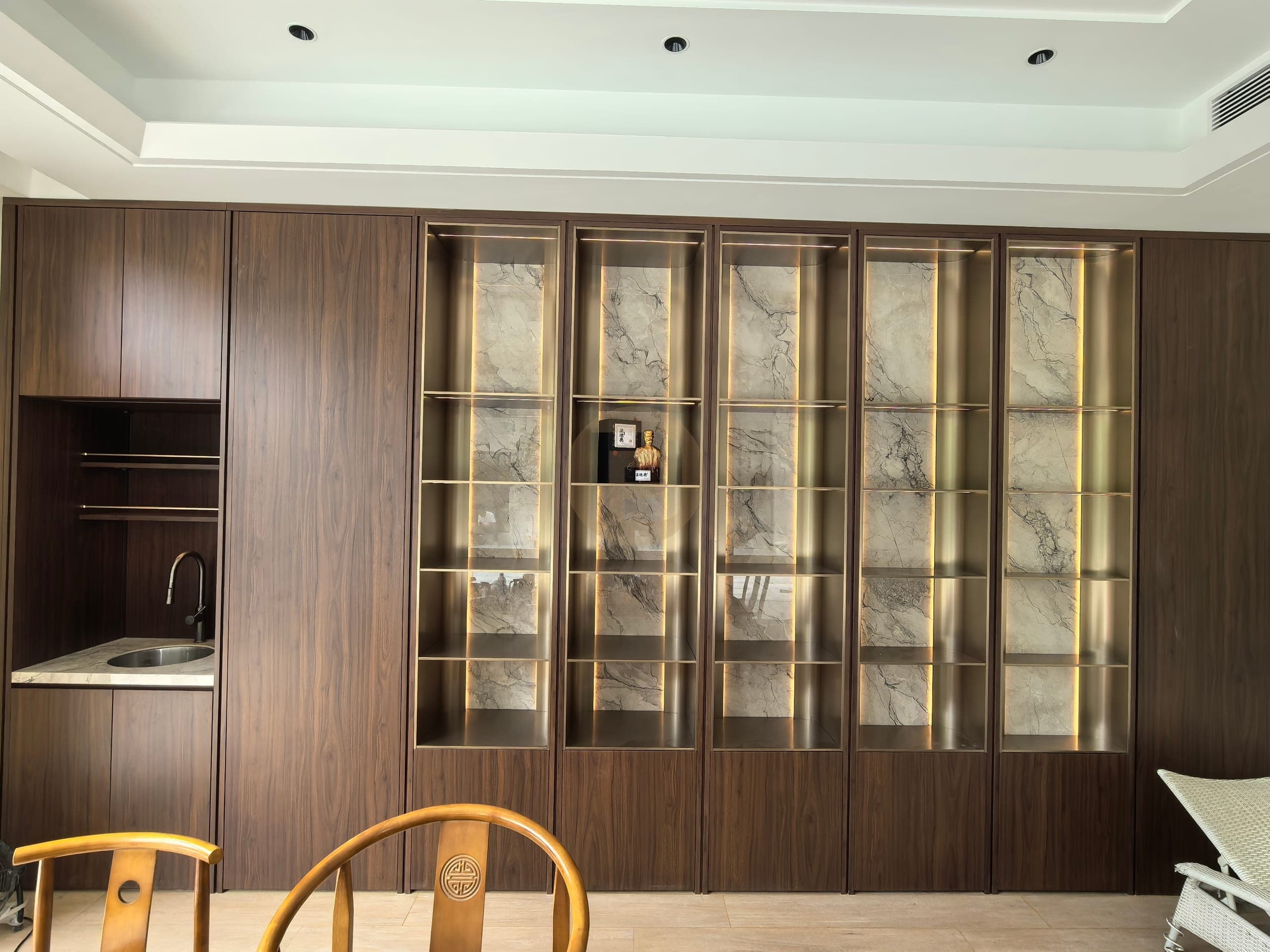Wood-look fitted wall combining lit glass display cabinets, closed storage and a small sink