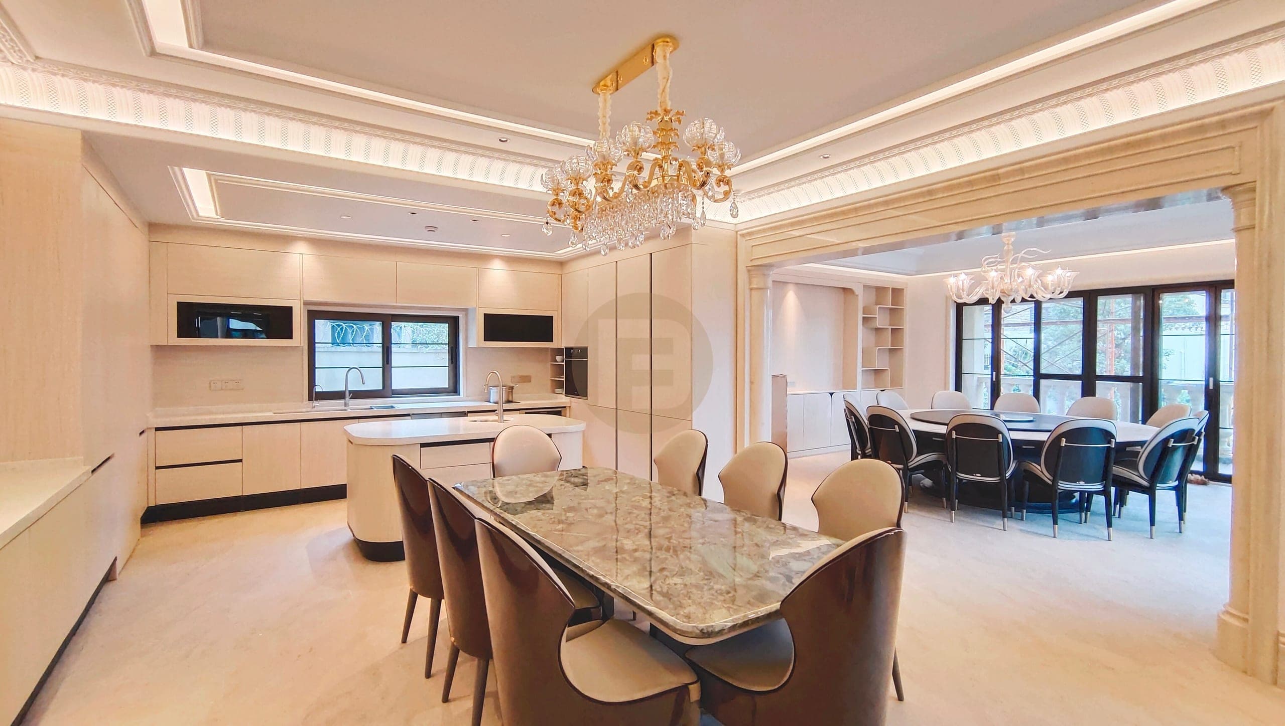 Cream wood-grain kitchen with a rounded island, marble-look dining table and formal dining room beyond