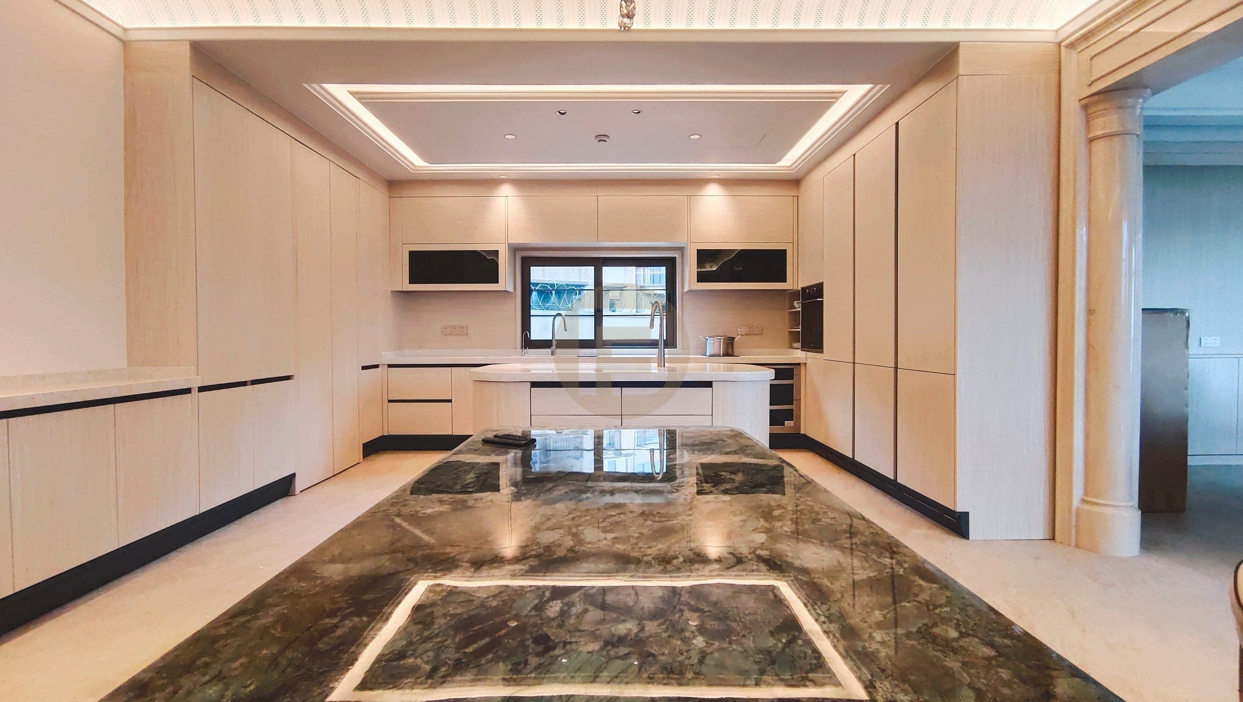 Cream wood-grain kitchen seen across a green stone-look island toward the window sink run
