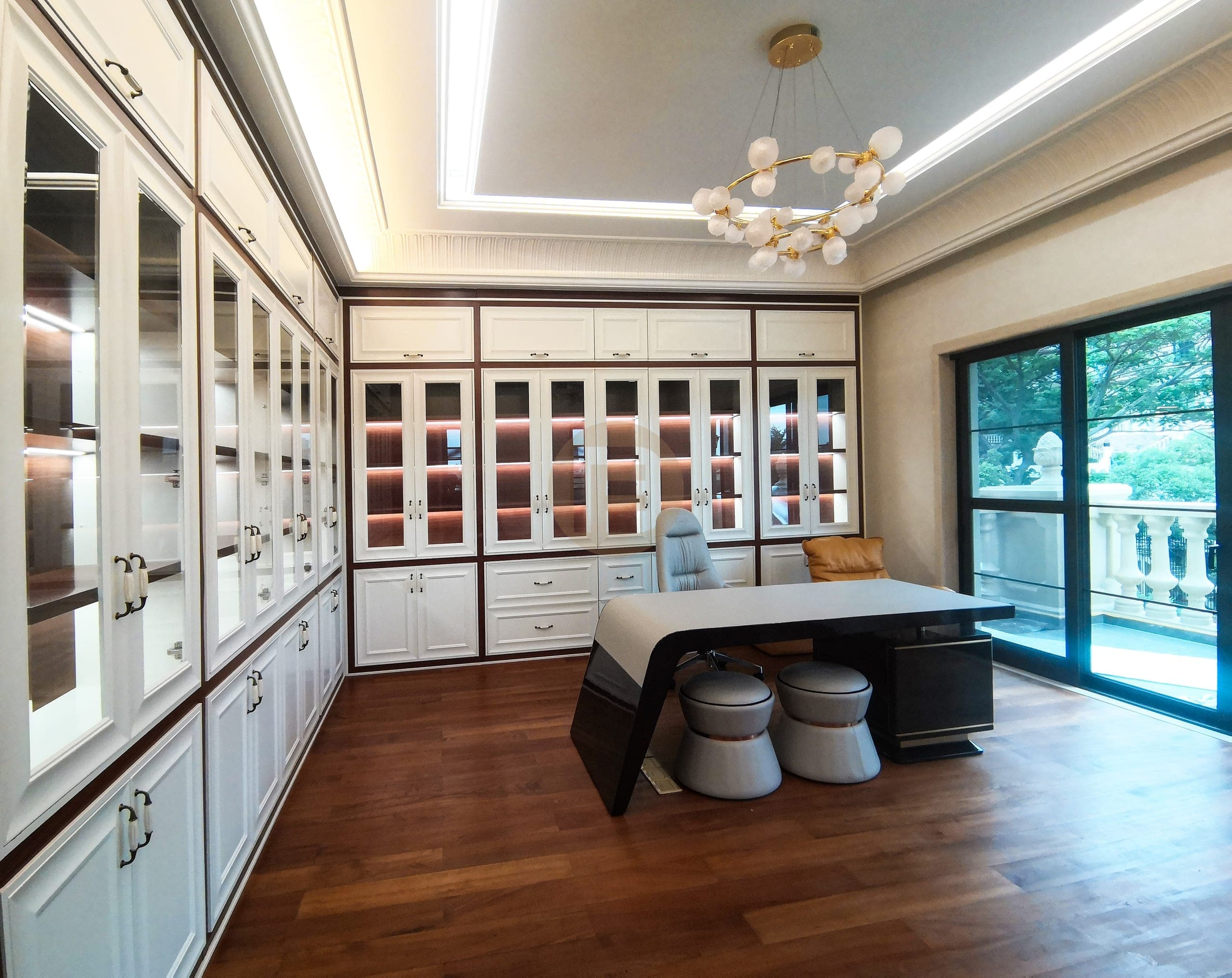 Study lined with white framed glass-front display cabinets and a desk by balcony doors