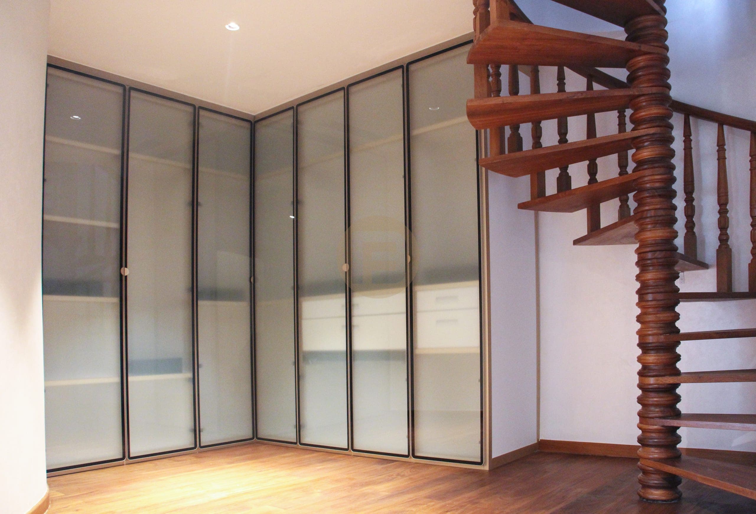 Frosted-glass corner wardrobe with slim dark frames beside a wooden spiral staircase