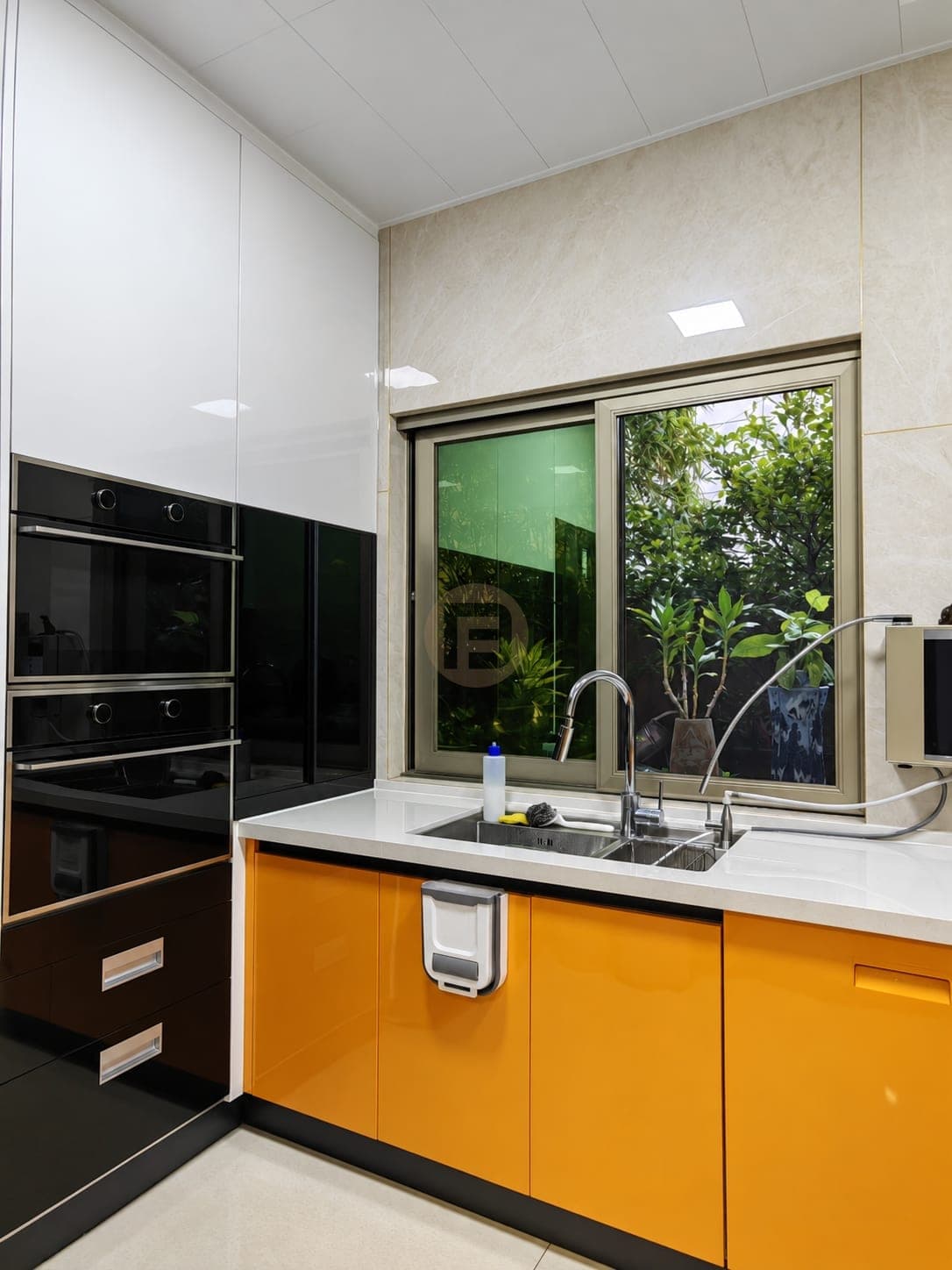 Orange sink run below a garden window beside black glass built-in ovens