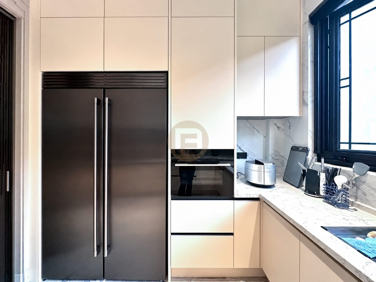 Frigorífico negro de dos puertas enmarcado por muebles crema junto al horno integrado